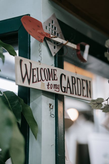 A close-up view of an indoor garden or plant nursery corner featuring a decorative wooden sign that reads 'Welcome to my GARDEN' hanging from a hook. The sign is painted in a rustic style with bold, d