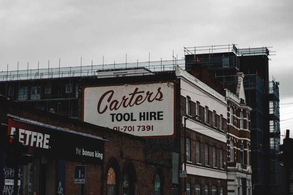 A brick building with a prominent white sign reading 'Carters TOOL HIRE' in large cursive and block letters, accompanied by a phone number beneath. The building features multiple windows with black fr